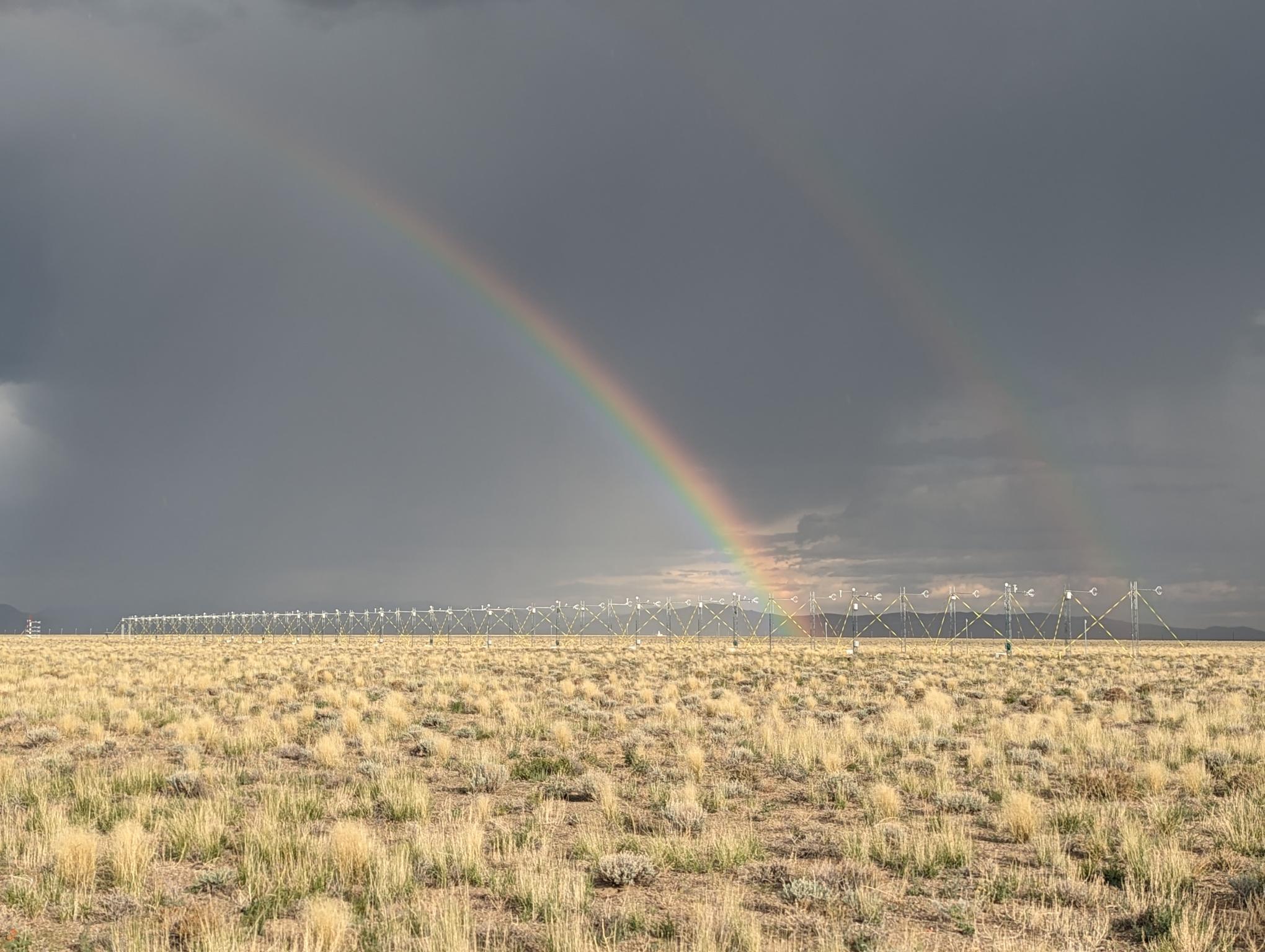 Two rainbows over a row of flux towers in a field. 