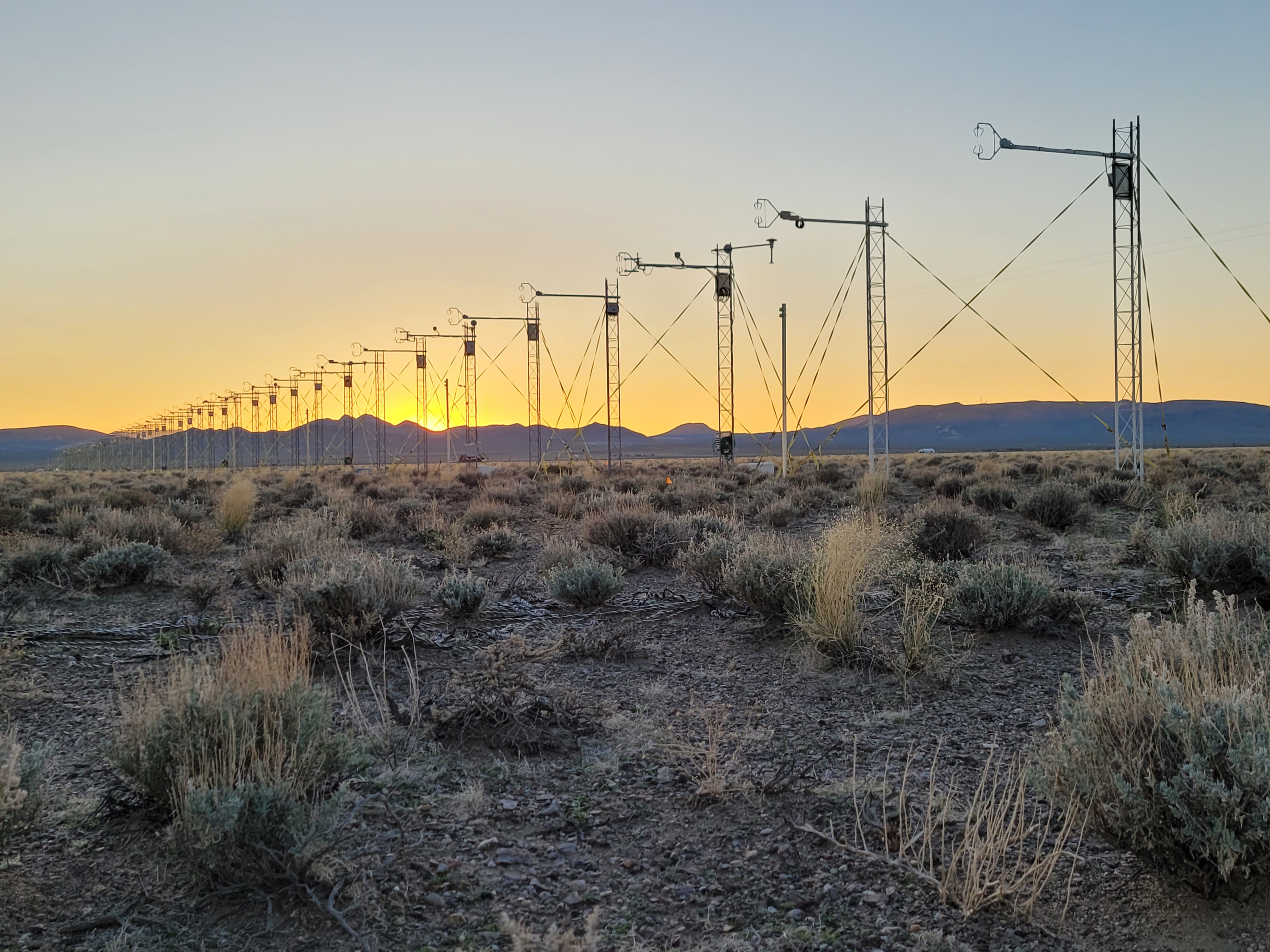 The sun setting behind a line of flux towers. 