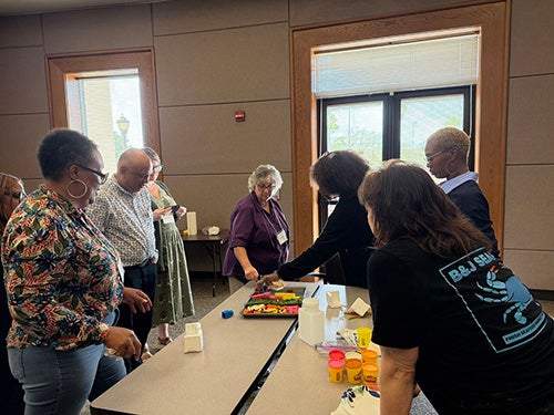 Several adults stand around a table that has play dough and other hands-on items for teaching children.