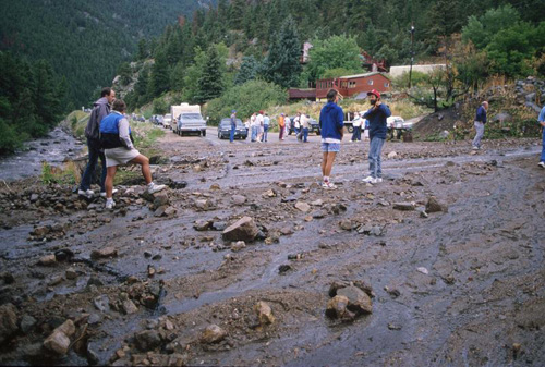 Photograph of people standing at a washed-out road after flood