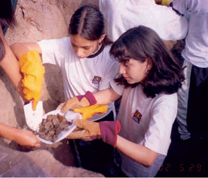 Photograph of teenagers standing in a hole, digging and collecting soil