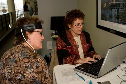 Photograph of two women, one taking a medical test, sitting in an office