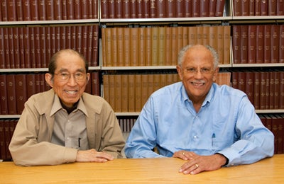 Two men sitting at table with book shelves behind them