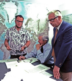 Photo of three men looking at documents