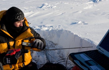 photo of man dressed in parka taking measurements in snow