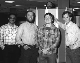 Photo of a group of men standing in front of a supercomputer