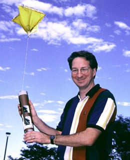 Photo of a man holding a small yellow balloon which is attached to a dropsonde