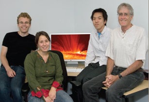 Photo of a group of four people with computer screen behind them