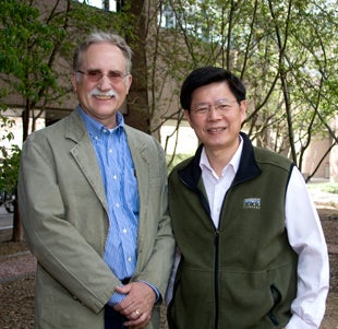Photo of two men standing in front of building and trees
