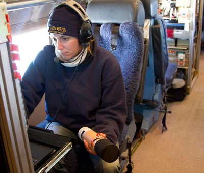 woman at control panel holds dropsonde in one hand