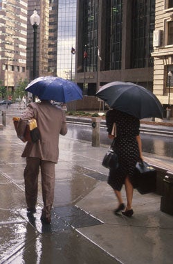 Photograph of people with umbrellas walking in rain