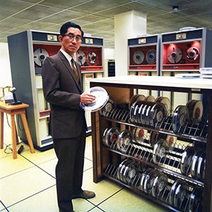 Akira Kasahara in computer room holding tapes.
