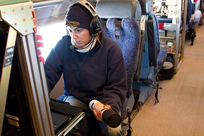 Laura Tudor holding a dropsonde and looking at a computer.