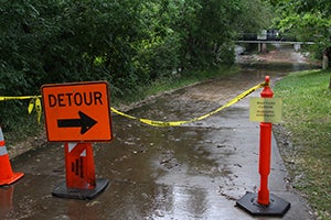 Orange sign that says "Detour" pointing people around a flooded walk way.