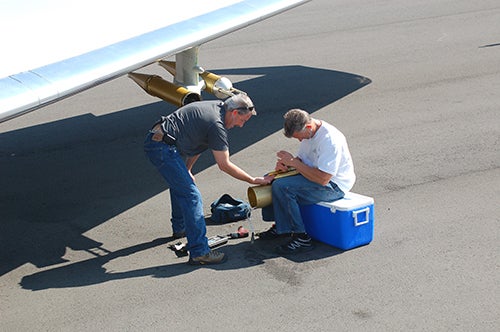 Two men working on instrument beneath the aircraft's wing.