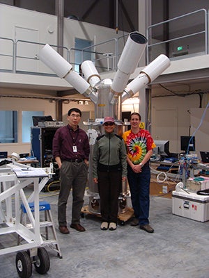 Three people standing in front of an instrument in a warehouse.