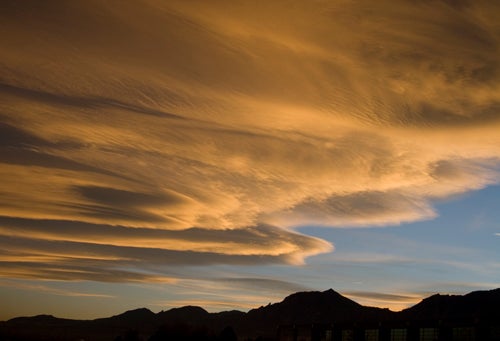 Golden lenticular clouds extending over the foothills.