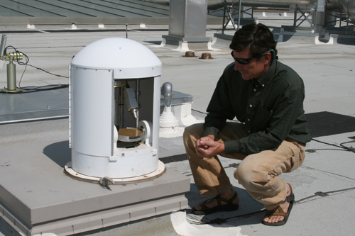 researcher crouches beside instrument encased in protective metal cover